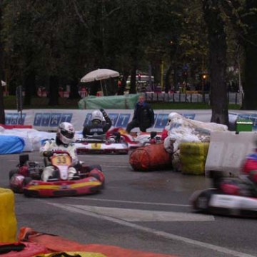 Go-kart race on outdoor track with drivers in helmets navigating through barriers.